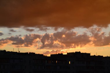 Parlak alışılmadık gün batımı şehir manzarası turuncu pembe ışınlar şehrin üzerinde. Acımasız panel binalar, koyu yağmur fırtınası bulutlarını aydınlatan turuncu-sarı ateşli gökyüzüne karşı siyah siluetler gibi görünür.