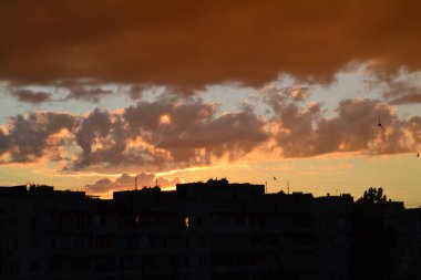 Parlak alışılmadık gün batımı şehir manzarası turuncu pembe ışınlar şehrin üzerinde. Acımasız panel binalar, koyu yağmur fırtınası bulutlarını aydınlatan turuncu-sarı ateşli gökyüzüne karşı siyah siluetler gibi görünür.