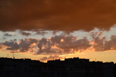 Parlak alışılmadık gün batımı şehir manzarası turuncu pembe ışınlar şehrin üzerinde. Acımasız panel binalar, koyu yağmur fırtınası bulutlarını aydınlatan turuncu-sarı ateşli gökyüzüne karşı siyah siluetler gibi görünür.