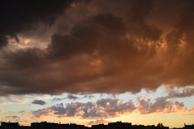 Bright unusual sunset city landscape orange pink rays above cityscape. Brutalist panel buildings appear as black silhouettes against a fiery orange-yellow sky dramatic lighting dark rain storm clouds clipart