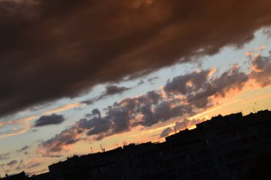 Parlak alışılmadık gün batımı şehir manzarası turuncu pembe ışınlar şehrin üzerinde. Acımasız panel binalar, koyu yağmur fırtınası bulutlarını aydınlatan turuncu-sarı ateşli gökyüzüne karşı siyah siluetler gibi görünür.