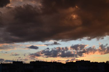 Parlak alışılmadık gün batımı şehir manzarası turuncu pembe ışınlar şehrin üzerinde. Acımasız panel binalar, koyu yağmur fırtınası bulutlarını aydınlatan turuncu-sarı ateşli gökyüzüne karşı siyah siluetler gibi görünür.