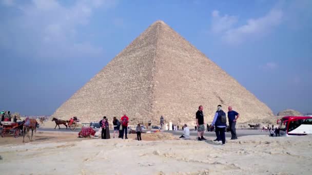 2022年12月 到楼下去 一群游客在吉萨的大金字塔前拍照 一个男人骑着骆驼穿过马路 金字塔被认为是七大奇迹之一 — 图库视频影像