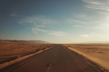 Çöle giden asfalt yol. Arka planda mavi gökyüzünün altındaki dağlar.