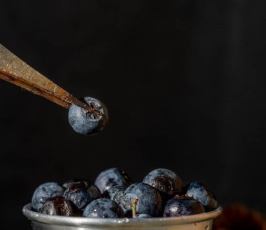 Masanın üzerinde yabanmersini dolu metal bir kase. Metal kaba yabanmersini koyarken bir klemp gözlenir..