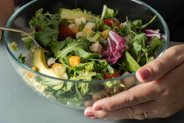 Salata, marul, kiraz, turp ve avokado. Bir bayanın elleri kaseyi tutuyor..