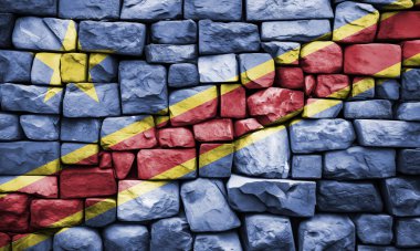 Çapraz mavi, sarı ve kırmızı çizgili engebeli taş bir duvarda resmedilen Kongo bayrağı ulusal gurur ve dayanıklılığı simgeliyor.