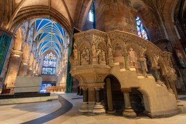 Edinburgh, Scotland - Nov 20, 2017: Majestic interior view of Edinburgh Cathedral featuring high ribbed vaulted ceilings, colorful stained glass windows, intricately carved stone columns, and a decorative stone pulpit clipart