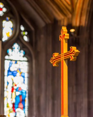 Kilisenin içinde altın dekoratif haç, bulanık renkli cam pencere zeminiyle, dini sanatları ve karmaşık tasarımı ön plana çıkarıyor.