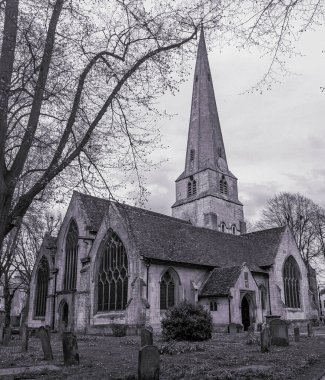 Cheltenham 'ın gri tonlu bir resmi, St Mary' s, Gotik mimarisini sergiliyor ve mezar taşları ve çıplak ağaçlar arasında ilham veriyor.