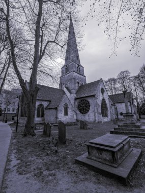 Cheltenham Minster 'ın gri tonlu manzarası, St Mary' s, belirgin kulesi ve bulutlu bir günde etrafındaki mezarlığıyla