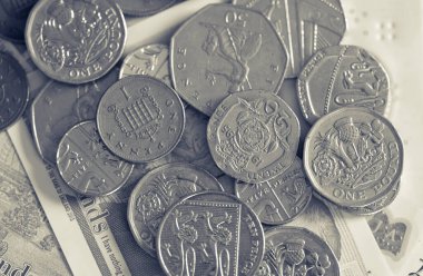 Bir peni, bir pound ve yirmi peni de dahil olmak üzere çeşitli İngiliz sikkelerinin yakın plan çekimleri, nostaljik tek renkli tonda solmuş banknotların üzerine saçıldı.
