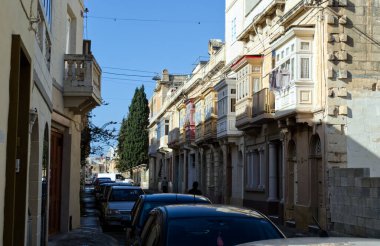 Malta 'da güneşli, dar bir caddenin klasik manzarası, adanın cazibesini tanımlayan eşsiz mimari ve renkli kapalı balkonları gözler önüne seriyor.