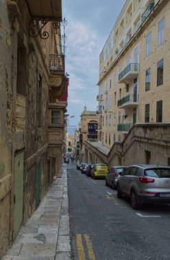 Tarihi Malta 'daki parke taşı caddesi, taş binalar ve işlenmiş demir balkonlarla kaplı - şehir mirası Akdeniz atmosferiyle buluşuyor