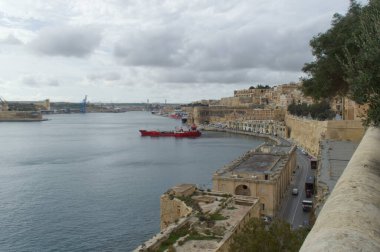 Valletta, Malta 'daki Grand Harbour manzarası - tarihi liman mimarisi, kırmızı gemi kenetlenmiş ve vinçlerle kenetlenmiş modern deniz faaliyetleriyle karşılaşıyor.