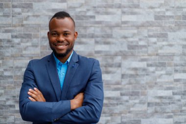 Portrait of confident african american male professional wearing blue suit using smartphone while standing against brick wall outside office