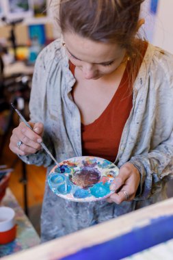 Female caucasian painter artist mixing paint for her next art piece in her professional studio