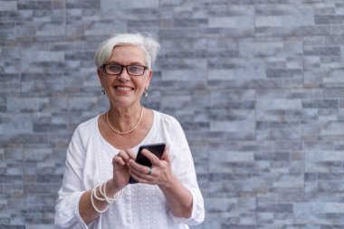 Portrait of smiling senior female executive with short hair wearing eyeglasses and standing against wall outside office