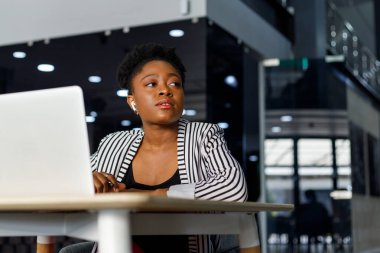 Cheerful african american young female professional laughing and looking away while working in modern corporate office