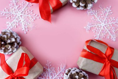 Pembe arka planda Noel ve Yeni Yıl modelleri. Kar taneleri, koniler ve hediye kutularından yapılmış çerçeve. Yukarıdan bak. Düz yatıyordu. Boşluğu kopyala.