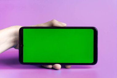 Kadının eli akıllı telefonu pembe arka planda yeşil ekranlı yatay pozisyonda tutuyor. Krom anahtar. Model.