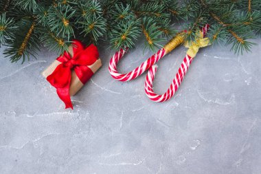 Kırmızı fiyonklu hediye kutuları, karamelli çubuklar ve çimento arka planda köknar dalları. Uzayı kopyala Noel ve Yeni Yıl konsepti. Kartpostal.