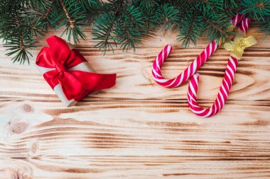 Kırmızı fiyonklu hediye kutuları, karamelli çubuklar ve ahşap arka planda köknar dalları. Uzayı kopyala Noel ve Yeni Yıl konsepti. Kartpostal.
