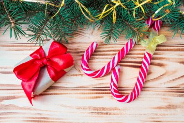 Kırmızı fiyonklu hediye kutuları, karamelli çubuklar ve ahşap arka planda köknar dalları. Uzayı kopyala Noel ve Yeni Yıl konsepti. Kartpostal.