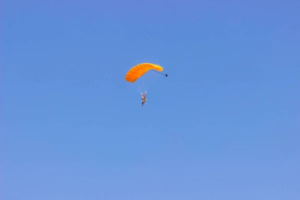 Mavi gökyüzünde turuncu paraşütü olan paraşütçü..