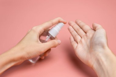 Elinde antiseptik olan bir kadın, arka planda pembe bir fonda avuca sıvı uyguluyor. Hijyen ve temizlik kavramı. Dezenfektan.