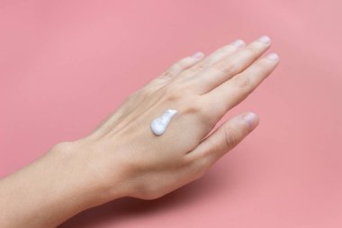 Pembe arka planda bir kadının elindeki krem. Cilt Bakımı Konsepti. Kozmetik reklamları.