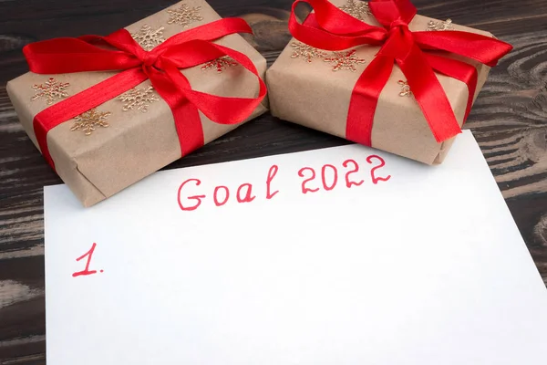 A sheet of paper with the inscription Goal 2022 and gifts on a wooden background. Close up.