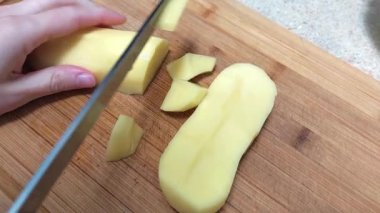 Bir kadının eli, tahta bir mutfak tahtasının üzerinde patatesleri bıçakla keser..