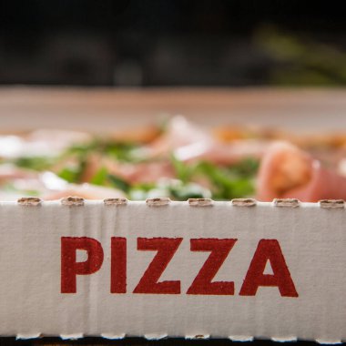 Pizzanın içinde ve dışında yazılı pizzanın olduğu mukavva, ahşap bir masada servis edilmeye hazır, izoalta