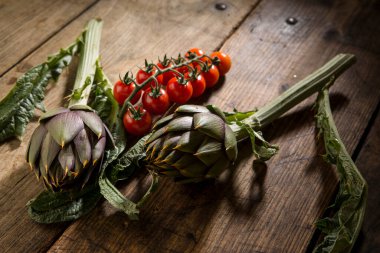 Bir demet kırmızı domates ve dikenli enginar ahşap masada izole edilmiş.