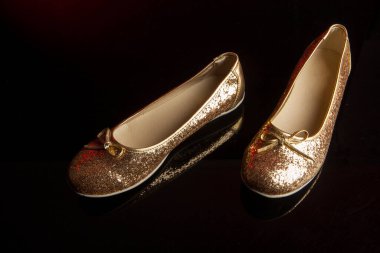 Yansıtıcı koyu bir arka planda parlak altın kadın ayakkabıları.