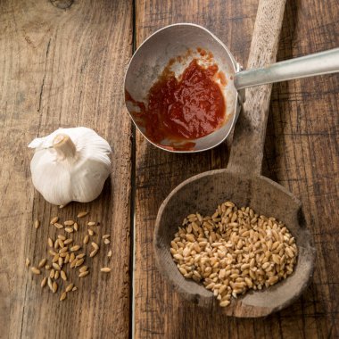 Antik kepçedeki buğday ve ahşap masadaki metal kepçe üzerindeki domates sosu.