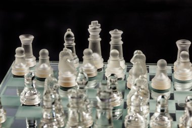 Satranç tahtasındaki cam satranç karanlık yüzeye yansıyor.