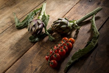 Bir demet kırmızı domates ve dikenli enginar ahşap masada izole edilmiş.