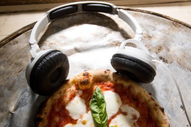 Masadaki margherita pizzasının üzerinde dinlenen beyaz modern kulaklıklar.