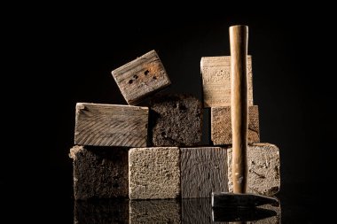 Kare tahta kütüklerin yanında çekiç, siyah arkaplanda izole edilmiş.