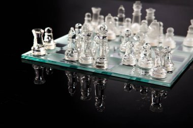 Satranç tahtasındaki cam satranç karanlık yüzeye yansıyor.