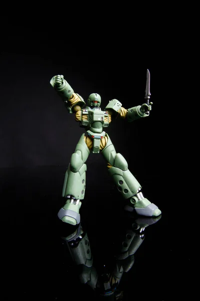Toy robot of green color wiggles sword , isolated on black background