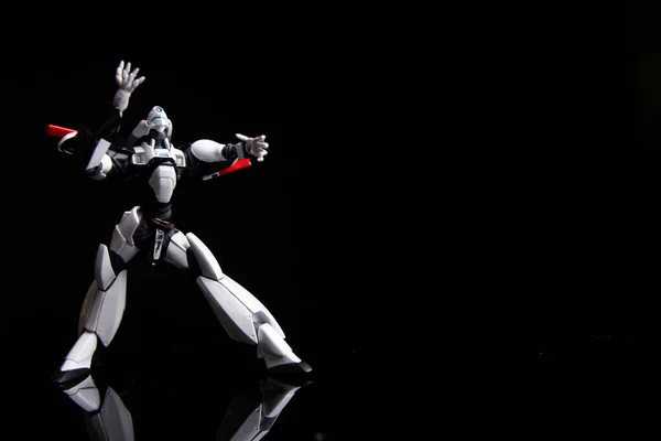 Red white toy robot moves in fighting pose, isolated on black background