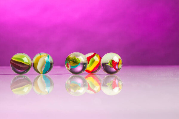 colorful marbles on reflective surface , isolated on fuchsia background