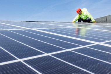 Üniformalı ve kasklı bir adam çatıda güneş panelleri var.