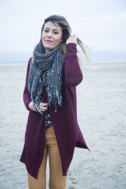 Güzel esmer kız, boynunda kahverengi süveter ve atkıyla, deniz kıyısına yakın.