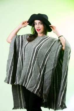 Yeşil arka planda şapkalı ve pançolu kadın kamerada mutlu görünüyor.