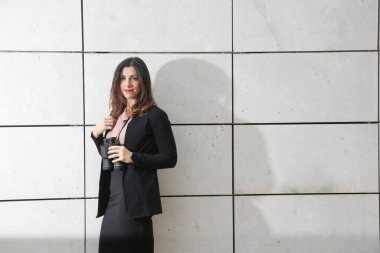 Siyah takım elbiseli esmer kadın yönetici, elindeki dürbünle diğer tarafa bakıyor, beyaz dikdörtgen duvar arka planında izole edilmiş.