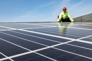 Kırmızı koruyucu kasklı, uzman tulumlu ve teknik gözlüklü işçiler bir binanın çatısına yerleştirilmiş fotovoltaik sistem üzerinde çalışıyorlar.